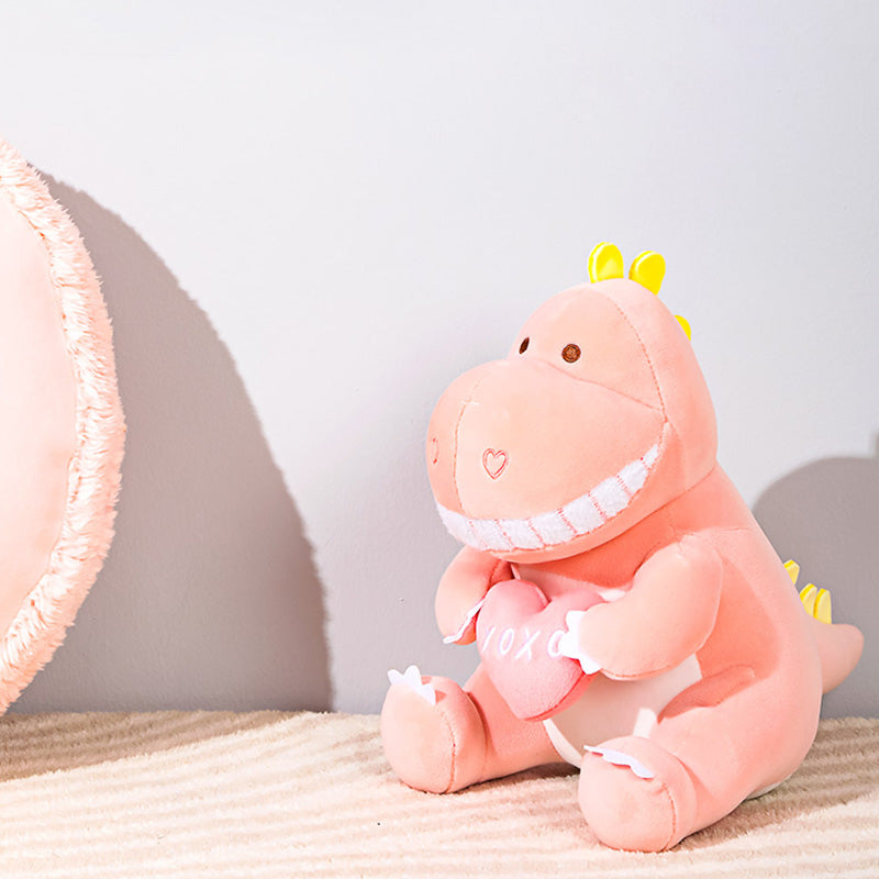 Draghetto rosa seduto con un cuscinetto a forma di cuore in mano e due cuoricini come narici della collezione Mini Family.